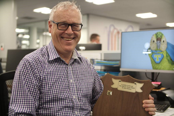 Executive Broker Murray Taylor holding a celebratory shield from the appreciative young brokers he mentors 